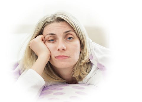 Kvinne i overgangsalderen som ligger sliten i sengen – illustrasjon av opplevelsen av hjernetåke